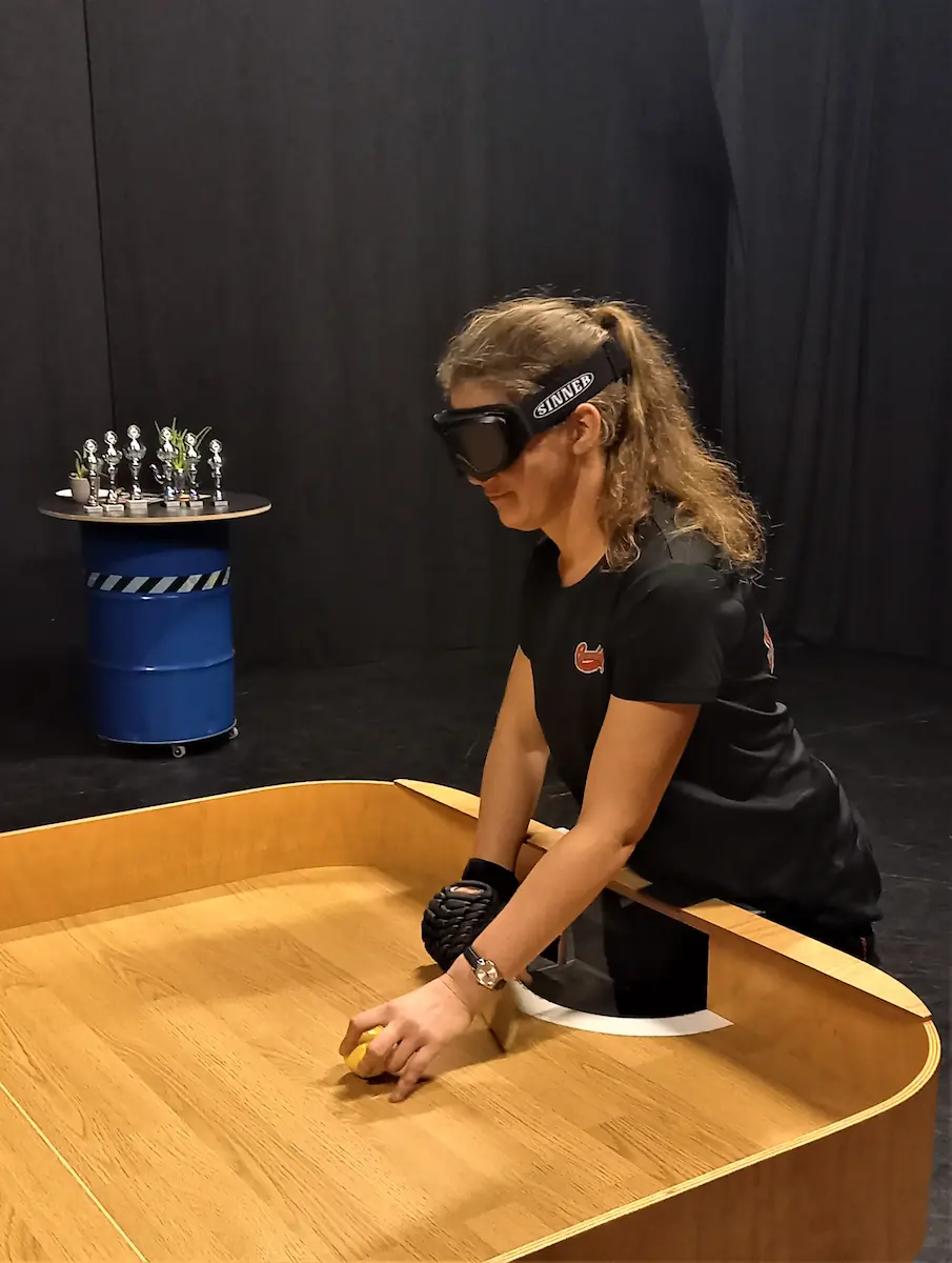 Iris staat met een geblindeerde showdownbril achter een houten showdowntafel en legt de gele bal klaar voor de opslag. Archiefoto van het Cannonballstoernooi 2022.